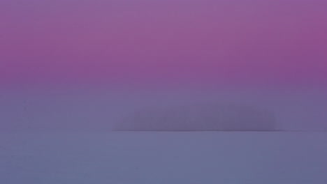 Shot-of-an-island-of-coniferous-trees-surrounded-by-snow-covered-plains-covered-with-dense-fog-in-timelapse-during-evening-time