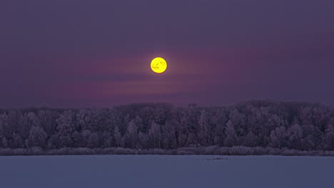 Full-moon-rising-above-the-winter-forest-landscape-and-into-the-misty-clouds---nighttime-time-lapse