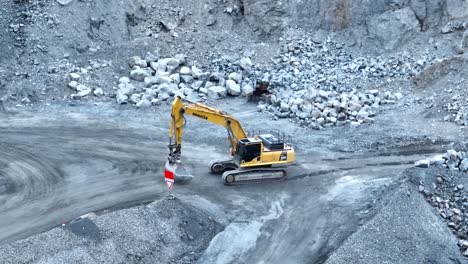 Aerial-panning-shot-of-excavator-driving-along-road-in-quarry,-then-shutting-down-for-the-day