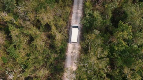 Mini-van-driving-on-a-sand-road-through-the-forest-of-Tulum,-Mexico-top-down-aerial-view