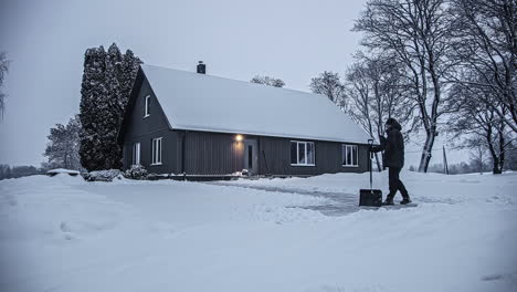 Man-shovels-snow-at-a-countryside-cottage-on-a-cold-day---time-lapse