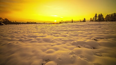 Timelapse-shot-of-snow-covered-rural-landscape-with-sun-rising-in-the-background-over-yellow-sky-during-morning-time