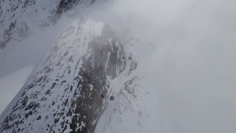 Moving-Gondolas-at-ski-lift-through-dense-fog-in-snowy-mountains-of-Austria---Aerial-top-down