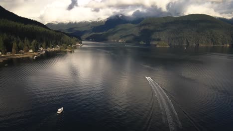 Extraordinary-Scene-of-a-Motorboat-driving-up-the-Indian-Arm-in-Deep-Cove-North-Vancouver-during-golden-hour-on-a-cloudy-day-with-beautiful-snows-capped-mountains