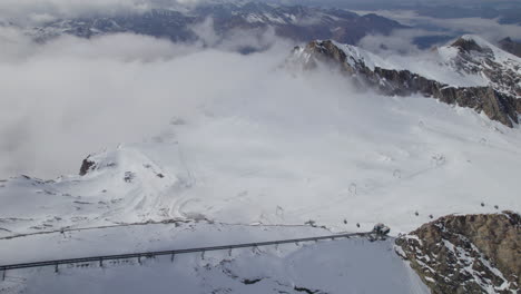 Luftaufnahme-Von-Oben-Nach-Unten-Von-Lift-Und-Wolkenmeer,-Die-Zwischen-Schneebedeckten-Bergen-In-Österreich-Hängen---Hochwinkelaufnahme-Von-Oben