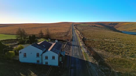Aerial-drone-video-footage-moving-slowly-down-a-country-road-and-passing-white-washed-Public-House,-high-on-the-Pennine-Hills,-UK