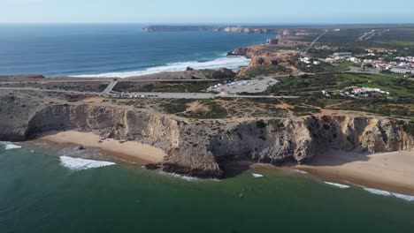 mareta-beach-in-portugal,-some-surfers-in-the-bay,-drone-shot-with-sunny-weather
