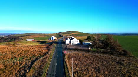 Aerial-drone-video-footage-moving-slowly-down-a-country-road-and-passing-white-washed-buildings,-high-on-the-Pennine-Hills,-UK