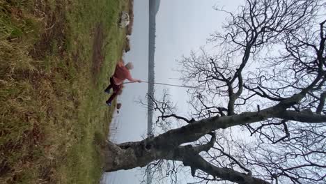 Man-enjoying-swing-by-lakeshore-Slow-motion-Vertical-Shot