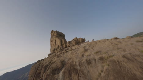 FPV-freestyle-aerial-view-up-and-over-Roque-Nublo-rock,-Extreme-mountain-summit,-Gran-Canaria