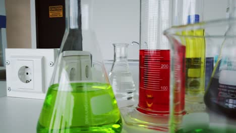 Panning-shot-of-lab-glasses-and-bottles-filled-with-liquid-in-various-colors