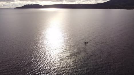 Aerial-drone-shot-of-a-small-sailboat-sailing-next-to-mountains-in-calm-water