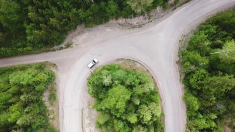 Birds-eye-view-of-a-Car-driving-on-a-half-circle-road-through-a-green-forest