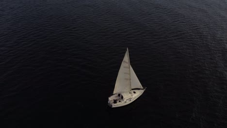 Bird's-aerial-view-of-small-sailboat-sailing-on-calm-sea-water,-minimal-travel