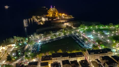Night-aerial-Hyperlapse-of-Corfu-old-Town,-fortress-and-green-square-with-lots-of-traffic