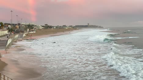 Unglaublich-Schöne-Sonnenuntergang-Himmel-Reflexionen-Von-Atlantischen-Ozeanwellen-Am-Carcavelos-Strand-In-Der-Nähe-Von-Lissabon,-Erstaunliche-Orangefarbene-Blaugrüne-Und-Blaue-Töne,-Einige-Leute-Gehen