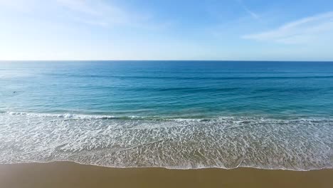Cool-ocean-waves-washing-against-Spanish-beach-golden-sandy-beachfront-aerial-view-dolly-left