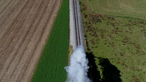 An-Aerial-View-From-Directly-Above-a-Steam-Train-Blowing-Smoke-and-Steam-at-the-Drone-as-it-Travels-Thru-the-Trees