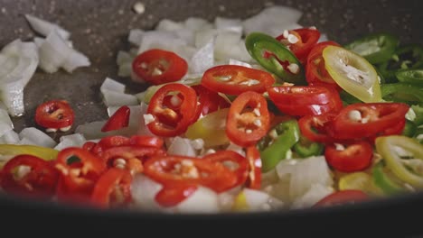 Adding-red-and-green-chopped-chili-to-a-pan-with-chopped-onion-and-oil,-close-up-view