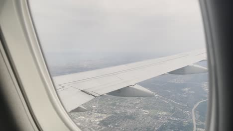 Blick-Aus-Einem-Flugzeugfenster,-Das-Tagsüber-über-Eine-Stadt-Fliegt