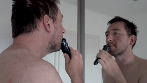 Mann,-Der-Seinen-Bart-Vor-Einem-Spiegel-Mit-Einem-Elektrorasierer-Rasiert