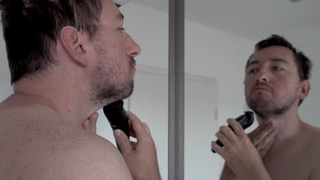 Man-shaving-his-beard-in-front-of-a-mirror-with-an-electrical-razor