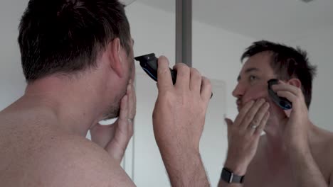 Hombre-Afeitándose-La-Barba-Frente-A-Un-Espejo-Con-Una-Maquinilla-De-Afeitar-Eléctrica