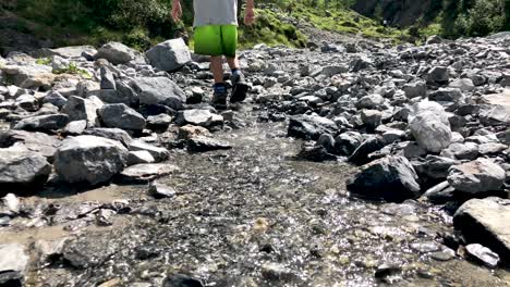 Cute-little-boy-walking-and-playing-with-stones-in-mountain-river-coming-from-a-waterfall