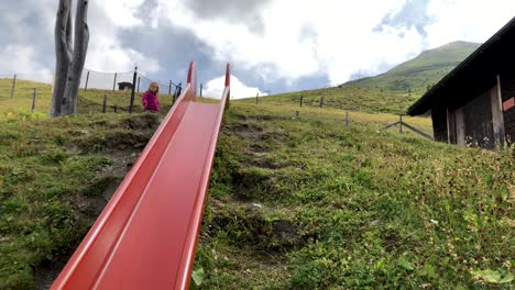 Cute-young-little-girl-approaching-and-sliding-down-a-slide-in-slow-motion-with-mountains-in-the-background