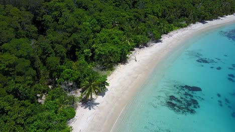 Drone-Volando-Sobre-Una-Perfecta-Playa-Tropical-De-Arena-Blanca-Con-Una-Exuberante-Jungla-En-Raja-Ampat,-Indonesia