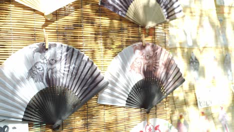 Traditional-Japanese-paper-folding-fans-hung-up-for-decoration-outside-midday-sunlight-in-Kyoto,-Japan-slow-motion-4K