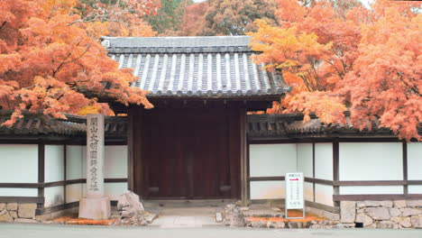 Small-gateway-entry-on-the-side-of-a-road-surrounded-by-orange-autumn-leaves-in-Kyoto,-Japan-meduim-shot