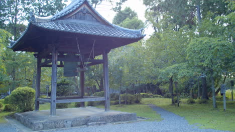 Big-Japanese-bell-surround-by-trees-in-a-beautiful-garden-in-the-background-in-Kyoto,-Japan-medium-shot-soft-lighting