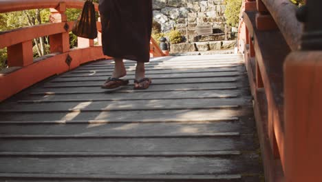 Slide-shot-of-a-person-wearing-a-Hakama-walking-over-a-bridge-in-a-Japanese-garden-in-Kyoto,-Japan-4K-slow-motion