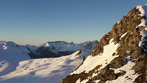 Disparo-De-Drones,-Camiones-De-Izquierda-A-Derecha-Detrás-De-Una-Cresta-De-Montaña-Con-Montañas-Cubiertas-De-Nieve-En-El-Fondo,-En-La-Plagne-En-Los-Alpes-Franceses