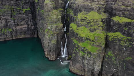 Faroe-Islands-sea-cliff-waterfall-aerial-reveal-in-remote-countryside,-overcast
