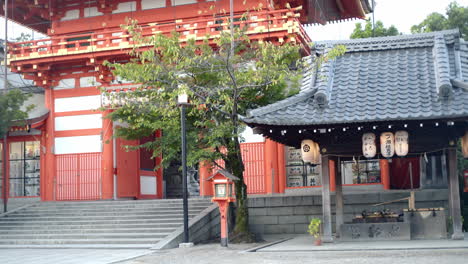 Agua-Saliendo-De-Un-Palo-De-Bambú-En-Una-Piedra-Tallada-Frente-A-Un-Gran-Santuario-En-Kyoto,-Japón-Iluminación-Suave