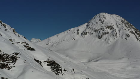 Drohnenschuss,-Der-Entlang-Einer-Schneebedeckten-Bergflanke-Vorwärts-Zu-Einem-Großen-Berg-Im-Hintergrund-Fährt