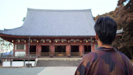 Guy-wearing-a-traditional-Japanese-traditional-Yukata-walking-towards-a-big-temple-in-Kyoto,-Japan-soft-lighting