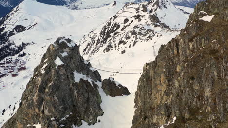 Drohnenschuss,-Der-Herausrollt,-Um-Eine-Drahtbrücke-Zwischen-Zwei-Berggipfeln-Zu-Enthüllen,-Und-Dann-Weitere-Schneebedeckte-Berge-In-La-Plagne,-Frankreich,-Enthüllt