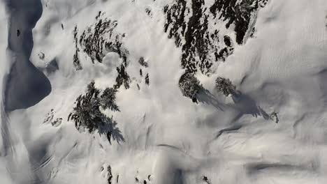 Drohnenschuss,-Der-Nach-Unten-Schaut-Und-Nach-Vorne-Fliegt,-Entlang-Einer-Schneebedeckten-Bergseite-Mit-Wunderschönen-Schneeformationen-Und-Felsen