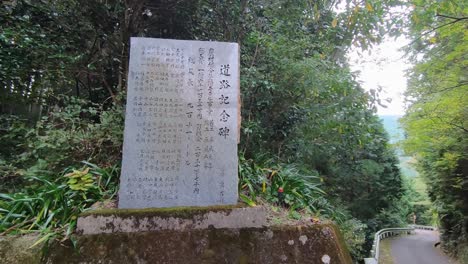 Plaque-With-Japanese-Writing-On-It-Next-To-Roadside-In-Forest