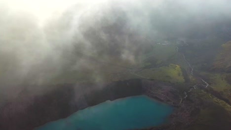 Aerial,-tilt,-drone-shot-through-low-clouds,-revealing-the-laguna-Humantay-lake,-in-Andes-mountains,-cloudy-day,-in-Cusco-region,-Peru