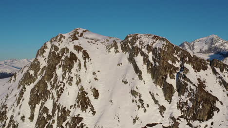 Die-Drohne-Schoss-Rückwärts-Von-Einem-Felsigen-Und-Schneebedeckten-Berg,-Um-Dahinter-Weitere-Berge-Zu-Enthüllen