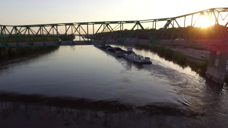 Aerial-dolly-under-bridge,-Cargo-boat-transportation-in-river,-Sunset-scene