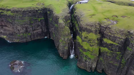 Waterfall-over-sea-cliff-edge-in-rural-Faroe-Islands,-aerial-landscape-reveal