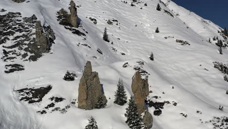 Drone-shot,-dolly-forward-and-up-over-a-snow-covered-mountain-side-with-interesting-rock-pinnacles-in-La-Plagne-,-French-Alps