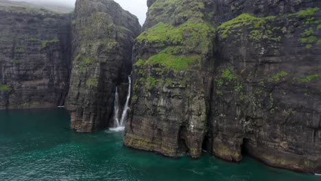Faroe-Island-sea-cliff-waterfall-aerial-reveal,-with-sea-bird-flying-towards-drone