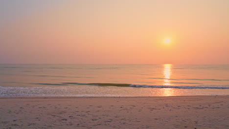 Romantische-Meerblickaufnahme-Eines-Orangefarbenen-Sonnenuntergangs-An-Einem-Klaren-Himmel-Und-Ruhige-Wellen,-Die-Langsam-An-Die-Küste-Kommen