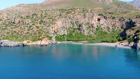Crystal-clear-turquoise-blue-river-water-at-the-isolated-beach,-surrounded-by-green-cliffs-of-island